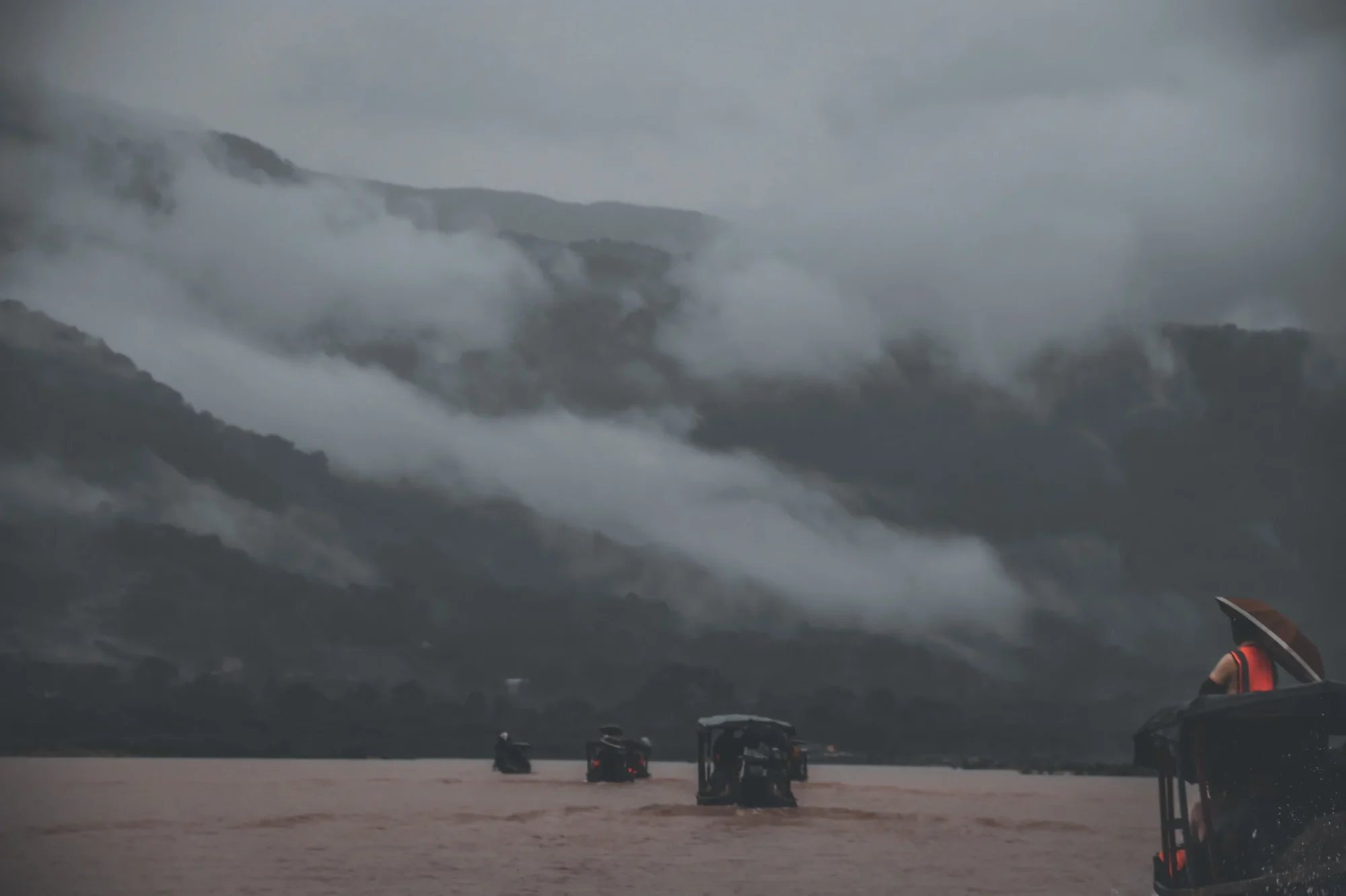 Cloud pouring over forested hills down to the water