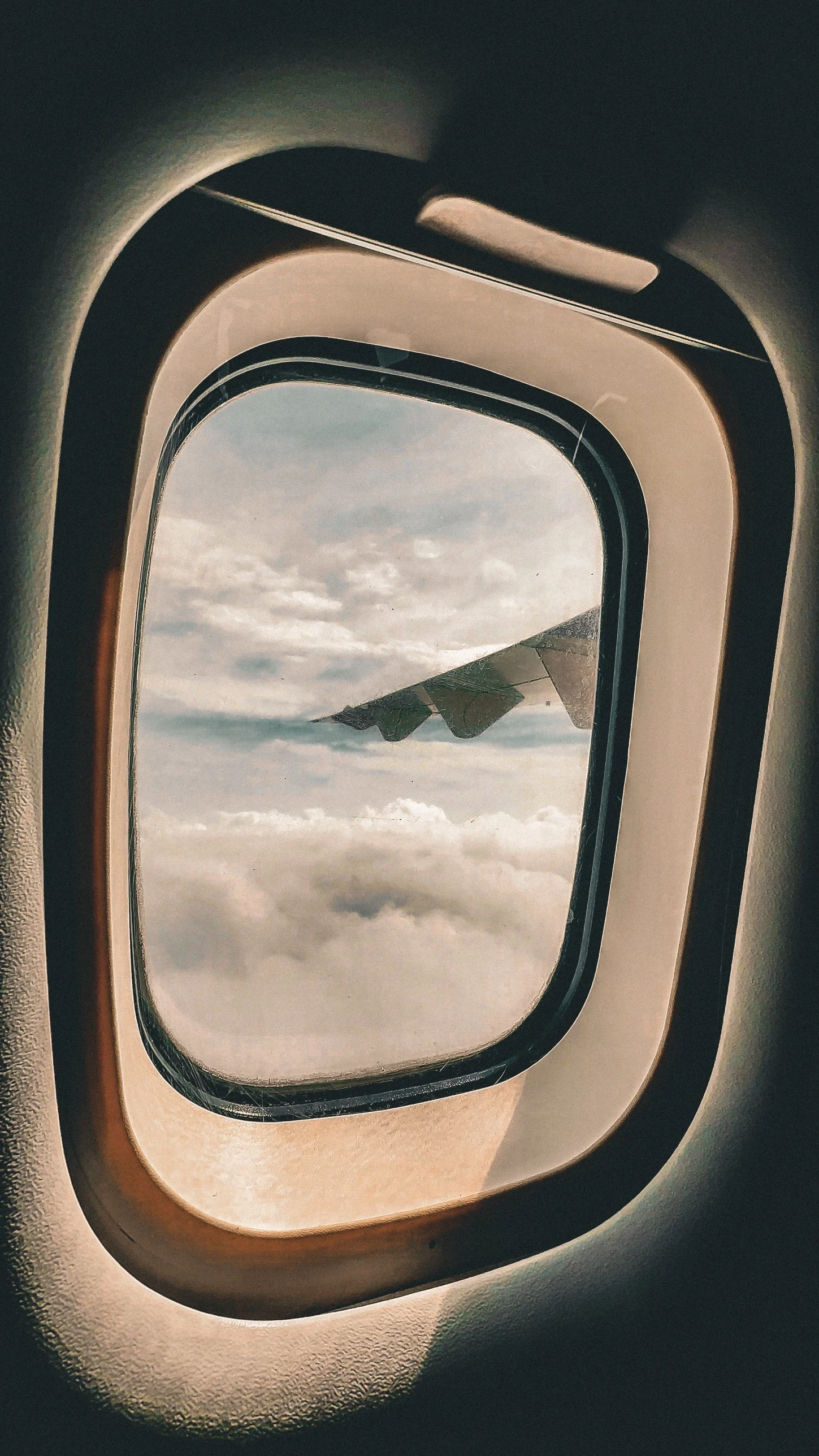 A wing seen through an aircraft window above a layer of cloud