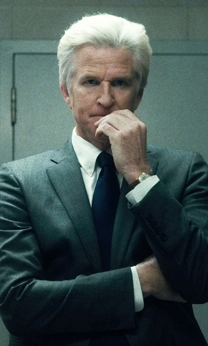 Doctor Brenner in a grey suit, hand at his mouth