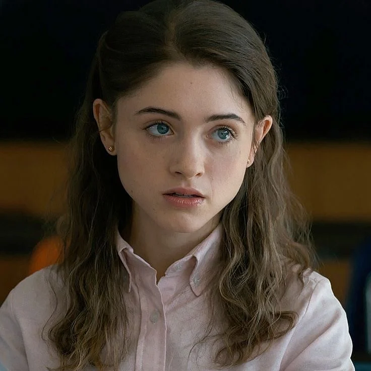 Nancy Wheeler in a pink shirt, looking off camera