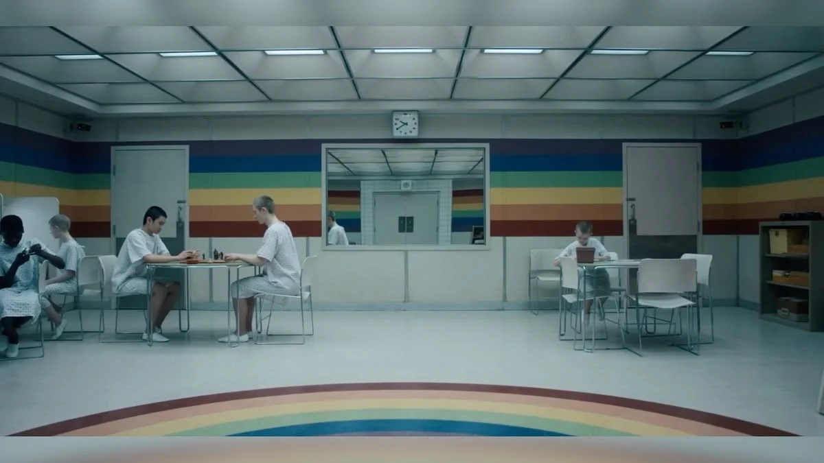 Children in hospital gowns at tables in a white room with a painted rainbow