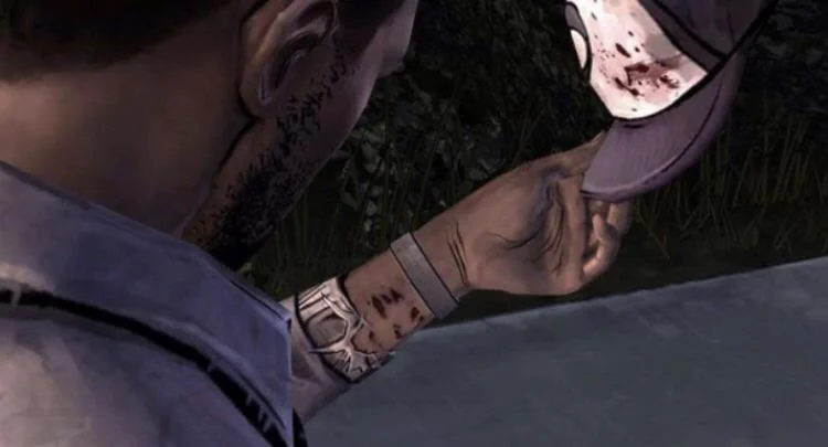 Lee's hand holding Clementine's cap, blood on the brim